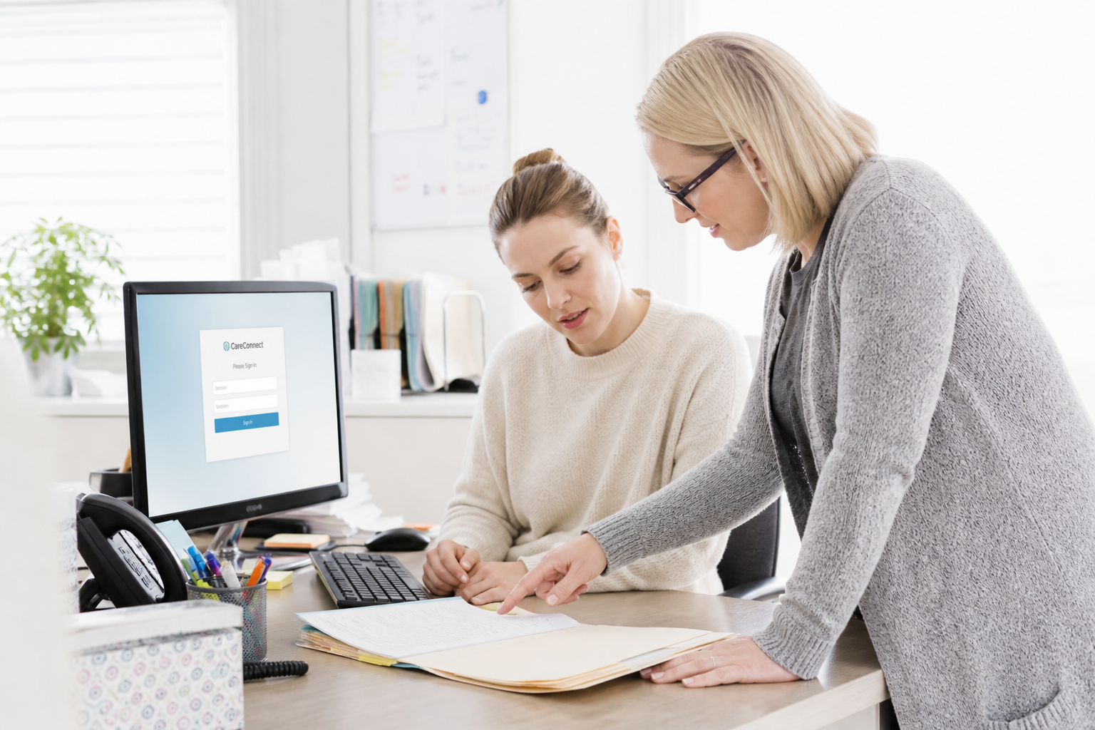 A scheduler and the agency's office manager stand beside a computer monitor showing a login screen, the manager leaning in