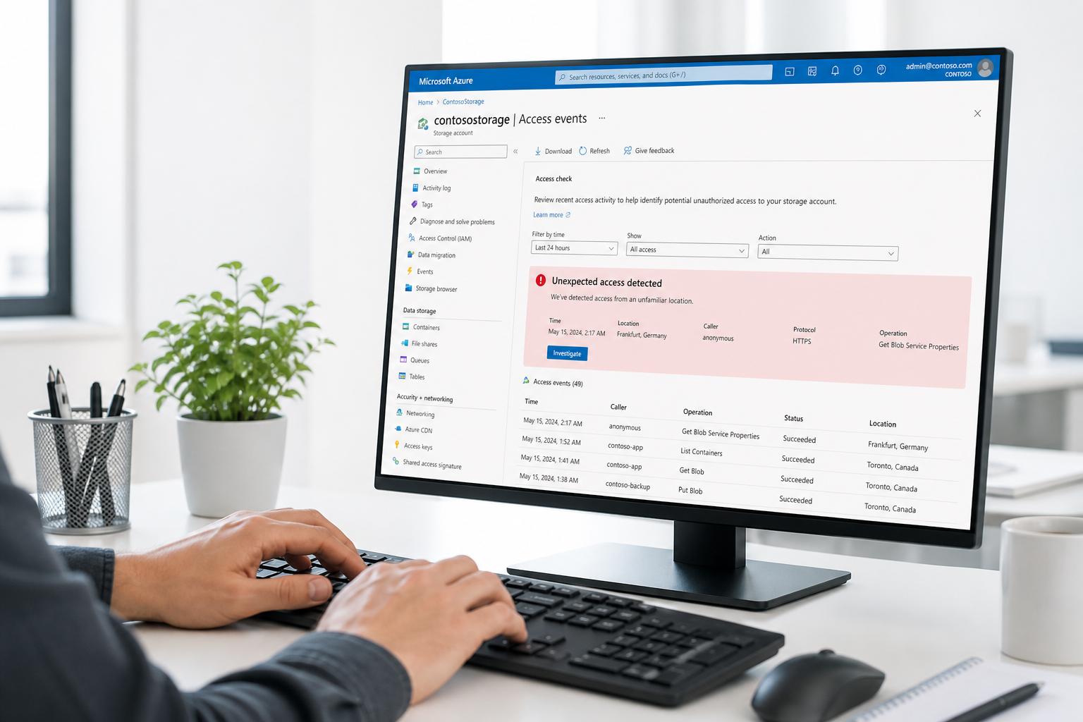 A system administrator's hands type at a keyboard in a bright office, the monitor showing the Microsoft Azure Storage portal