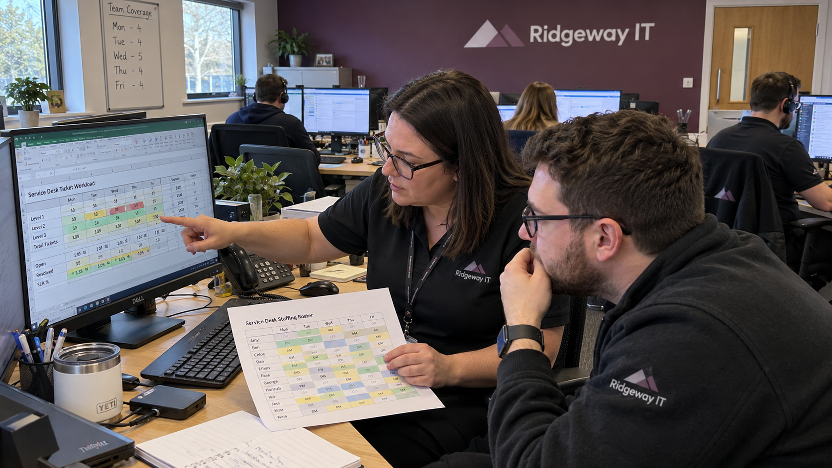 Service desk staffing review with a workload spreadsheet and printed roster at an MSP workstation