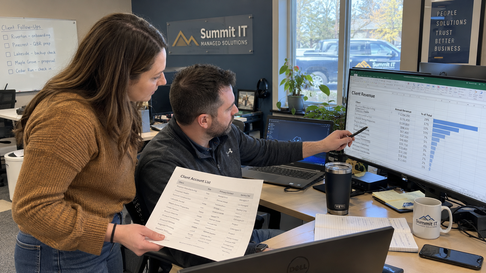 Two people reviewing a client revenue spreadsheet and a paper client account list in an MSP office.