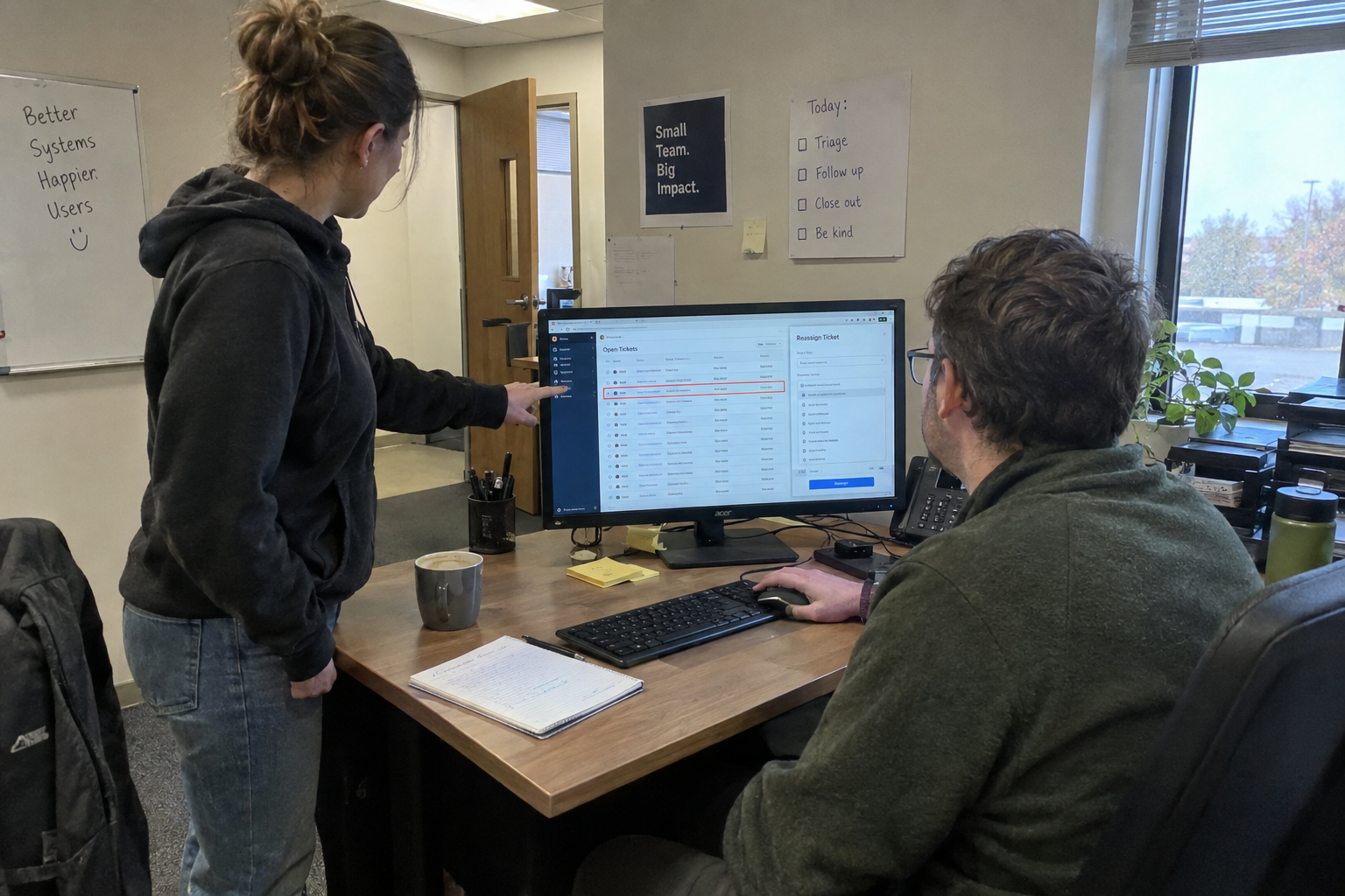 Two MSP technicians review open tickets and a reassignment panel at a workstation.