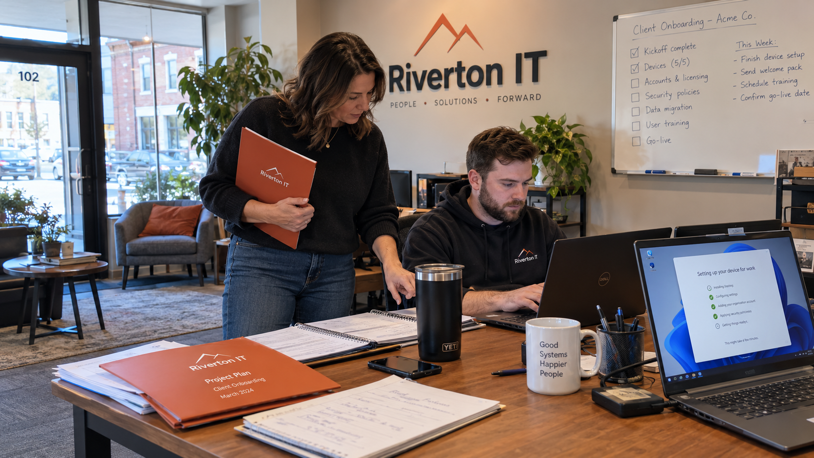 Engineer sets up a client laptop as the owner reviews work covered by the waived MSP onboarding fee.